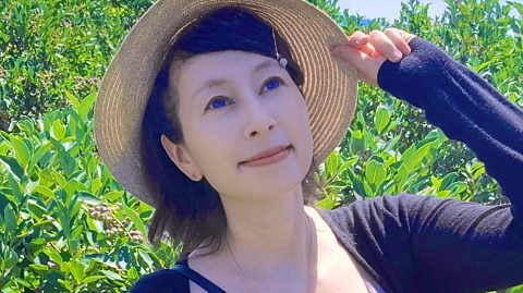 Composer Laura Shigihara posing in a sun hat in front of some green bushes