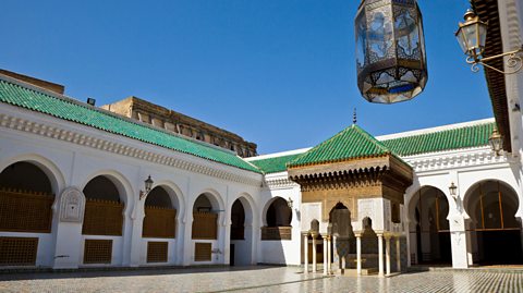 Exterior of the al-Qarawiyyin Library, with white arched walls, green roof tiles and an ornate gold and white tiled entrance