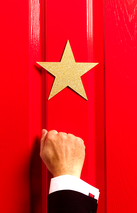 A hand knocking on a red door with a golden star. 