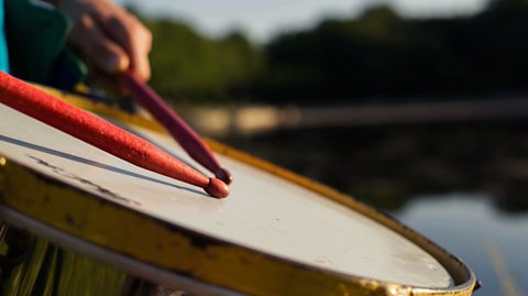 A close up image of a drum being played with two red drumsticks.