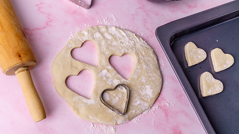 A heart-shaped cookie-cutter on some dough. 