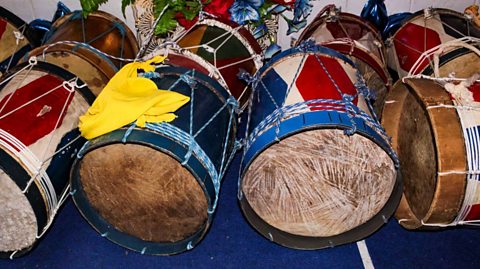 Eight brightly coloured drums on a blue floor ready to be used in a carnival.