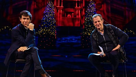 Alastair Campbell and Rory Stewart sitting on chairs facing the camera and smiling. Both are wearing dark suits and have lit up Christmas trees behind them.