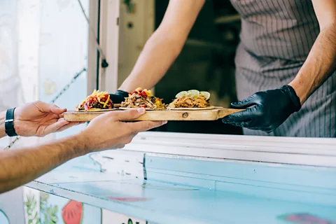 Getty Images Man handing tray of tacos to another man from taco truck (Credit: Getty Images)