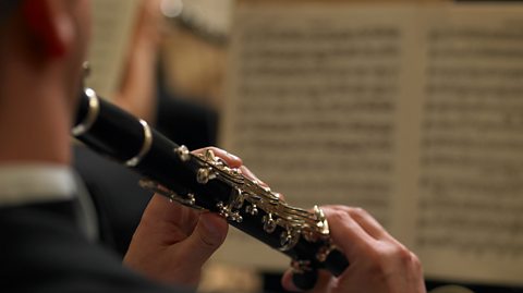 A rear view photo of the hands of a male clarinet player with sheet music visible.