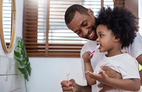 A dad with his daughter brushing her teeth.