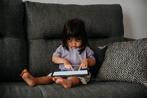 A girl sat on the sofa with a tablet computer.