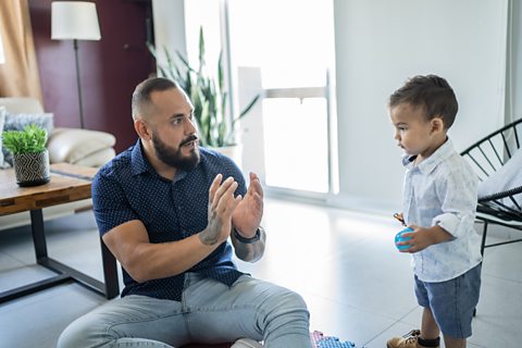 A dad sat on the floor talking to his toddler son.