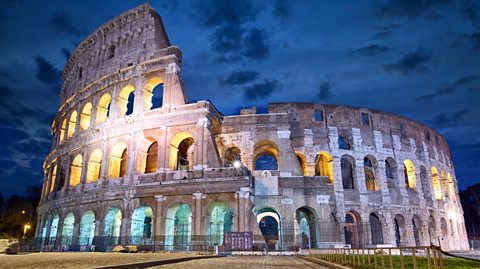 The Colosseum, a large ancient stone amphitheatre, under the night sky.