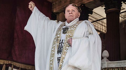 Actor Anthony Hopkins, dressed as a Roman emperor, with his fist clenched and raised above his head as he looks forward.