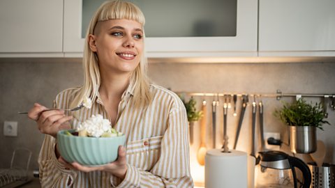 A young (gen z) person eats a bowl of salad topped with cottage cheese