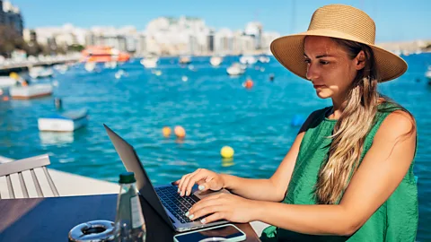 Getty Images Woman in a hat working on her laptop by the ocean (Credit: Getty Images)