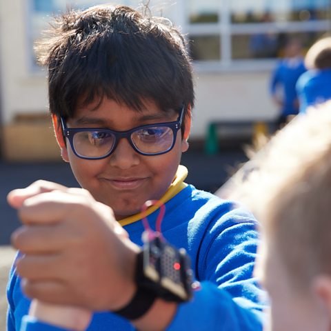 A student wearing a micro:bit on his wrist grips the hand of another boy