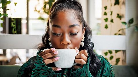 A woman in a green jumper drinks a cup of coffee