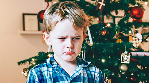 Young boy looking sad at Christmas in front of tree