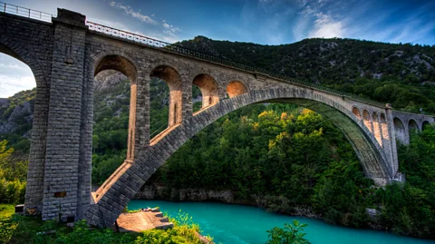 Getty Images Jembatan Solkan melengkung secara dramatis di atas Sungai Soča, menciptakan latar belakang yang menakjubkan untuk hiking, kayak, dan piknik (Kredit: Getty Images)