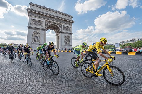 Tour de France cyclists race past the Arc de Triomphe. The leading rider is wearing the traditional yellow shirt denoting the fastest overall time.