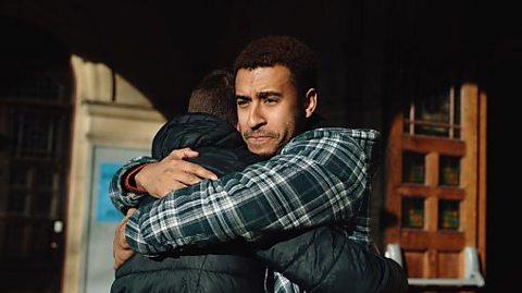 An older person comforts a younger one with a hug