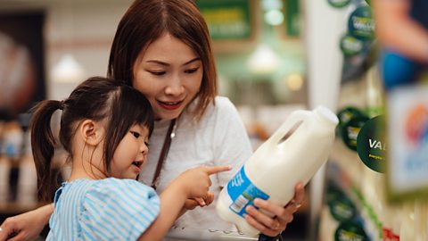 Young Asian mother and daughter reading nutrition label on milk bottle while shopping in supermarket.