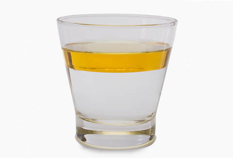 A glass containing oil and water demonstrating the different densities of the liquids. The oil has settled in a single layer on top of the water. The liquids aren't mixed together.