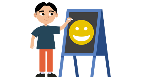 A boy drawing a smiley face on a blackboard