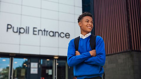 Teenage boy standing and smiling outside of his school entrance