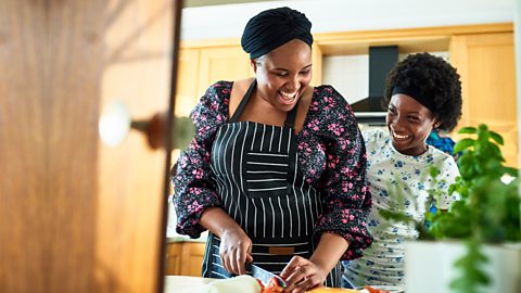 Black woman and girl laughing in the kitchen, chopping vegetables and making lunch.