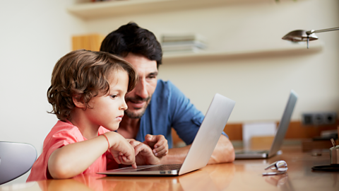 A dad and his son stoop over a laptop screen, looking up some facts