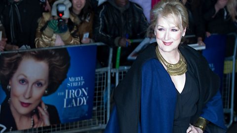 Actor Meryl Streep in a blue cape and blue dress, with fans behind her.