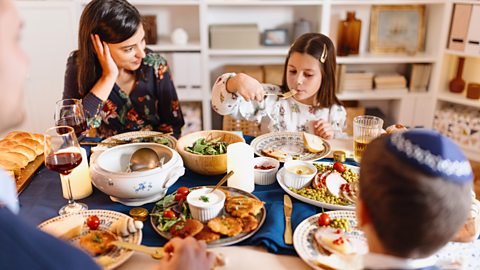 Jewish girl sitting at the table with her family and eating traditional food during Hanukkah.