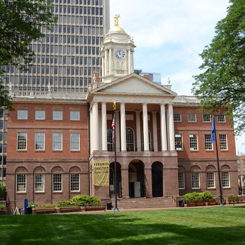 A large brick building with a white clock tower and white columns surrounding the porch entrance 