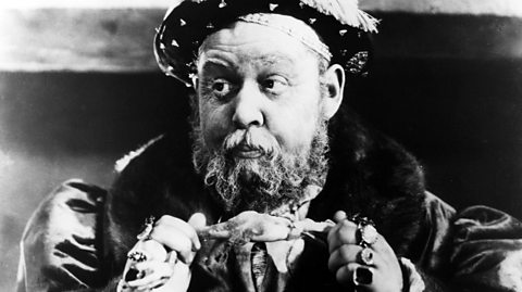 Actor Charles Laughton dressed as Henry VIII, eating a chicken thigh.