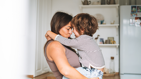 A pregnant mum cradles her young son in her arms, he has thrown his arms over her shoulders.