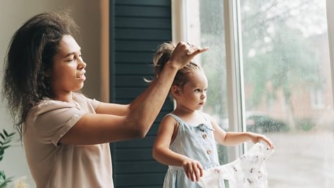 A mum ties her young daughter's hair into a high ponytail.