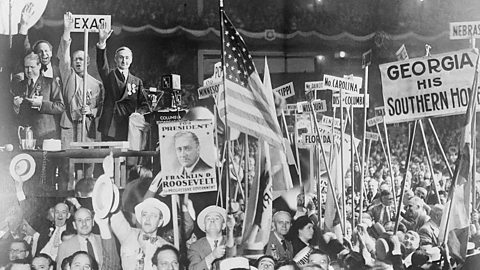 A crowd of smartly dressed men waving American flags and holding banners in support of FDR