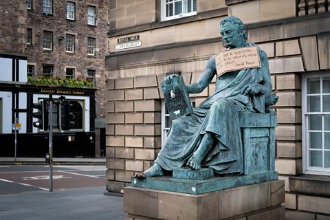 Ìomhaigh de David Hume ann an Dùn Èideann le placard a' togail fianais air a mhuin