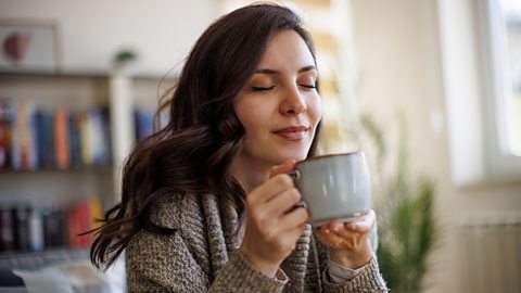 Woman sits on the sofa with a hot drink