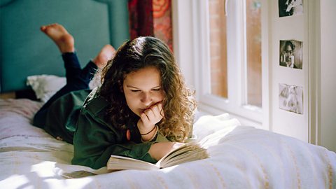 Teenage girl laying on her bed while reading a book