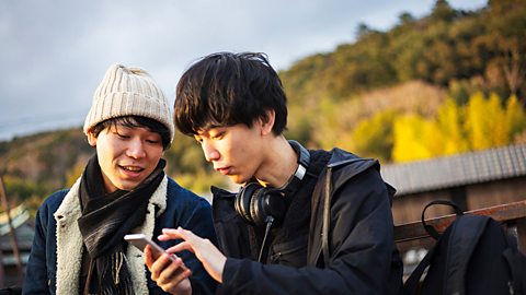 Two male teenagers with one using his smartphone