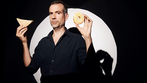 Chris Van Tulleken stands with a shop-bought sandwich in one hand and a doughnut in the other 