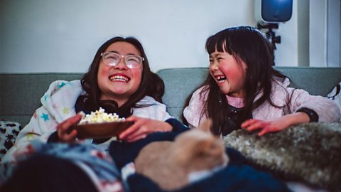 Sisters eating popcorn and laughing on the sofa