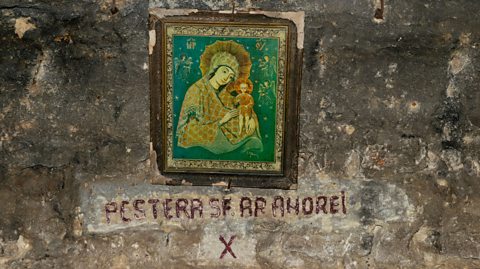 A framed religious painting affixed to a rough stone wall