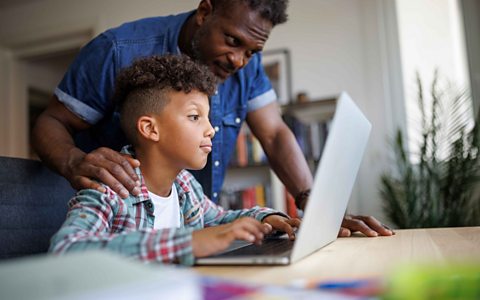 A image of a father helping his son with his homework on a silver laptop. 