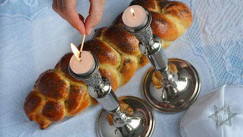 Shabbat candles being lit, with challah bread and a kippah nearby