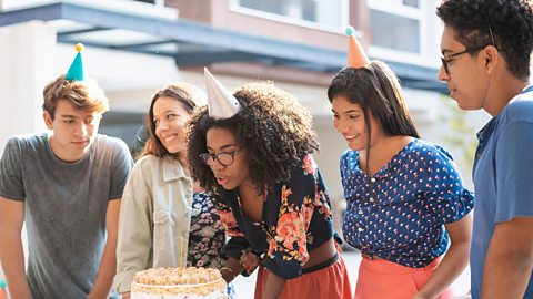 Group of teenagers watching their female friend blow out candles on a birthday cake