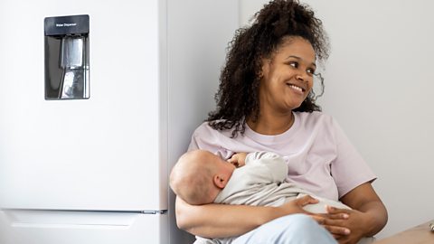 A woman smiles, breastfeeding her baby.