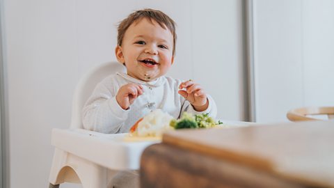 A smiling baby with a messy face sits in a high chair.