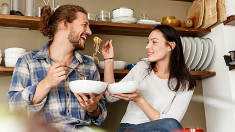 Couple sitting on a kitchen counter eating spaghetti together