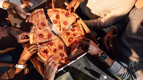 Getty Images People at table grabbing slices of pizza (Credit: Getty Images)