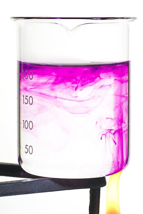 A beaker containing a crystal of potassium permanganate is heated and the coloured fluid inside shows convection currents.
